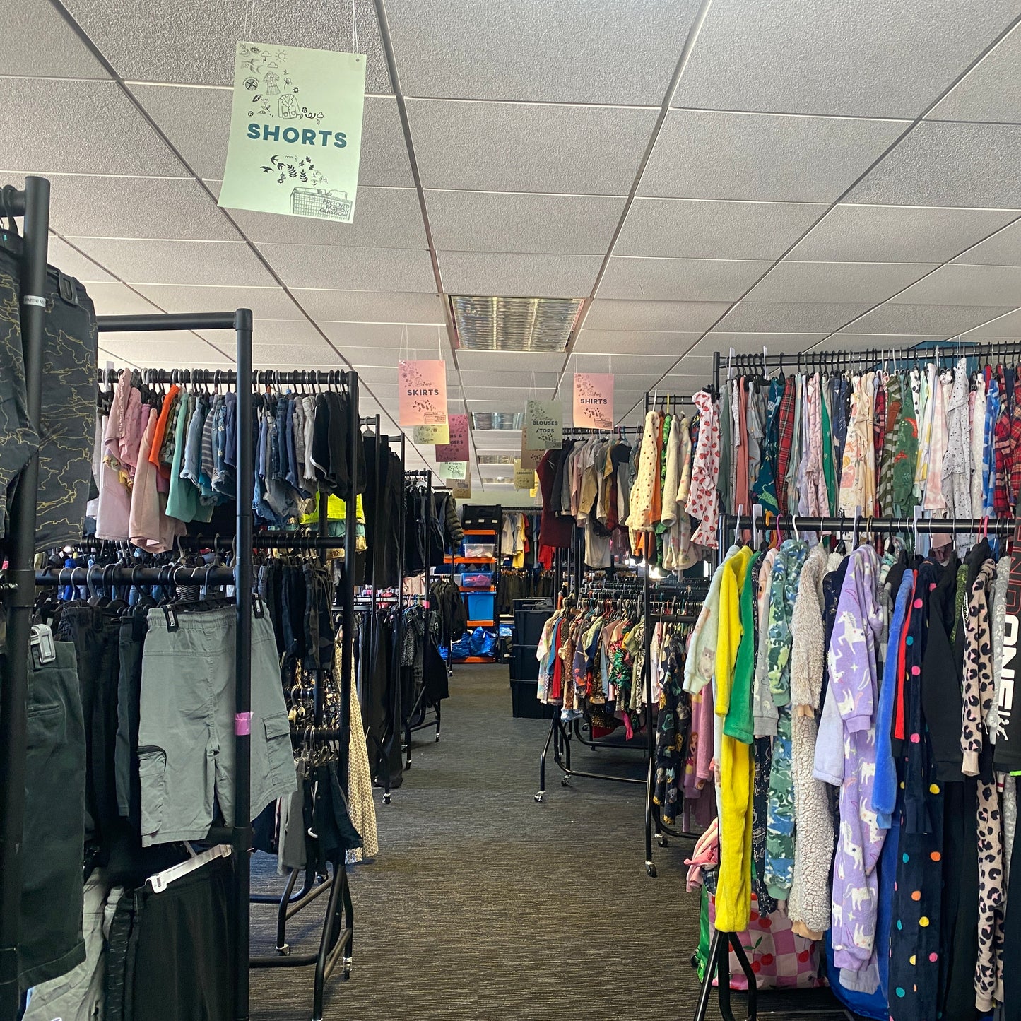Clothing store with racks of clothes and signs on the ceiling