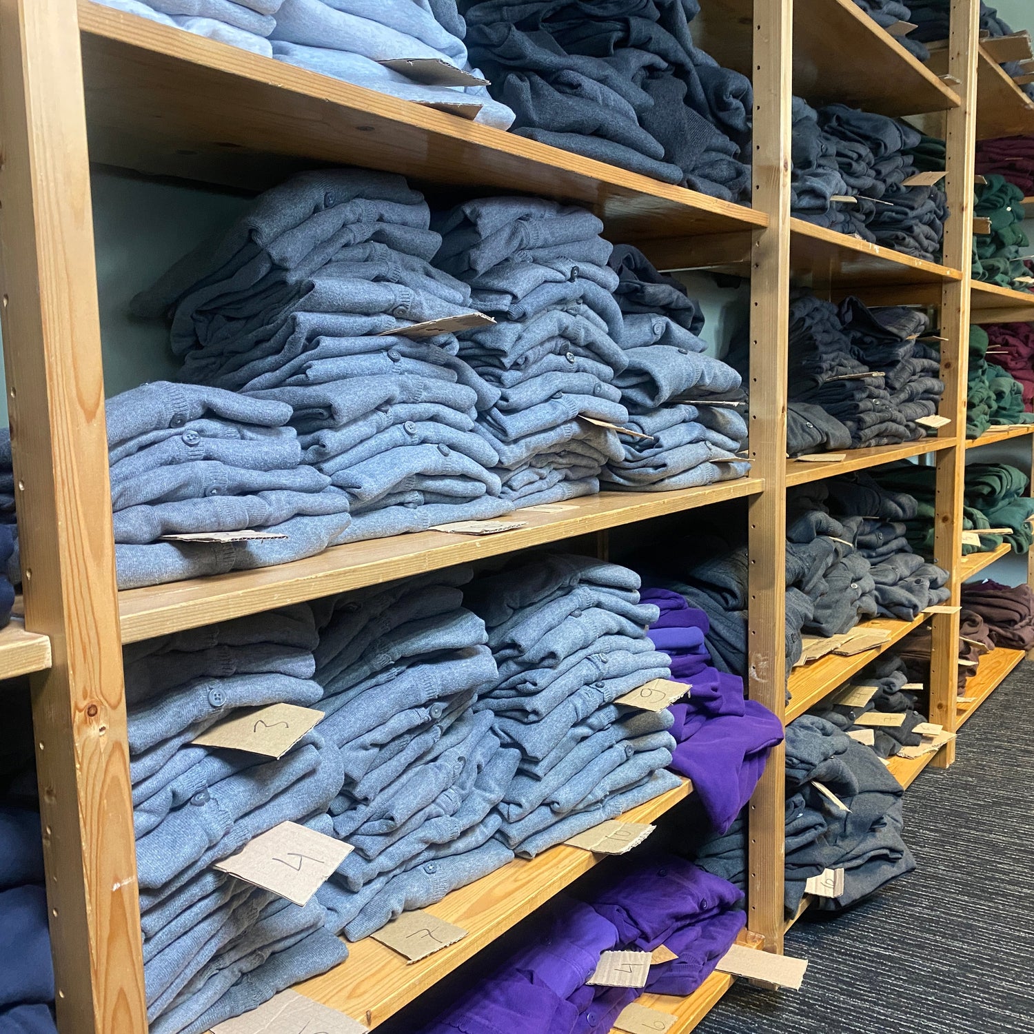 Stacks of folded preloved clothes on wooden shelves in a storage room.